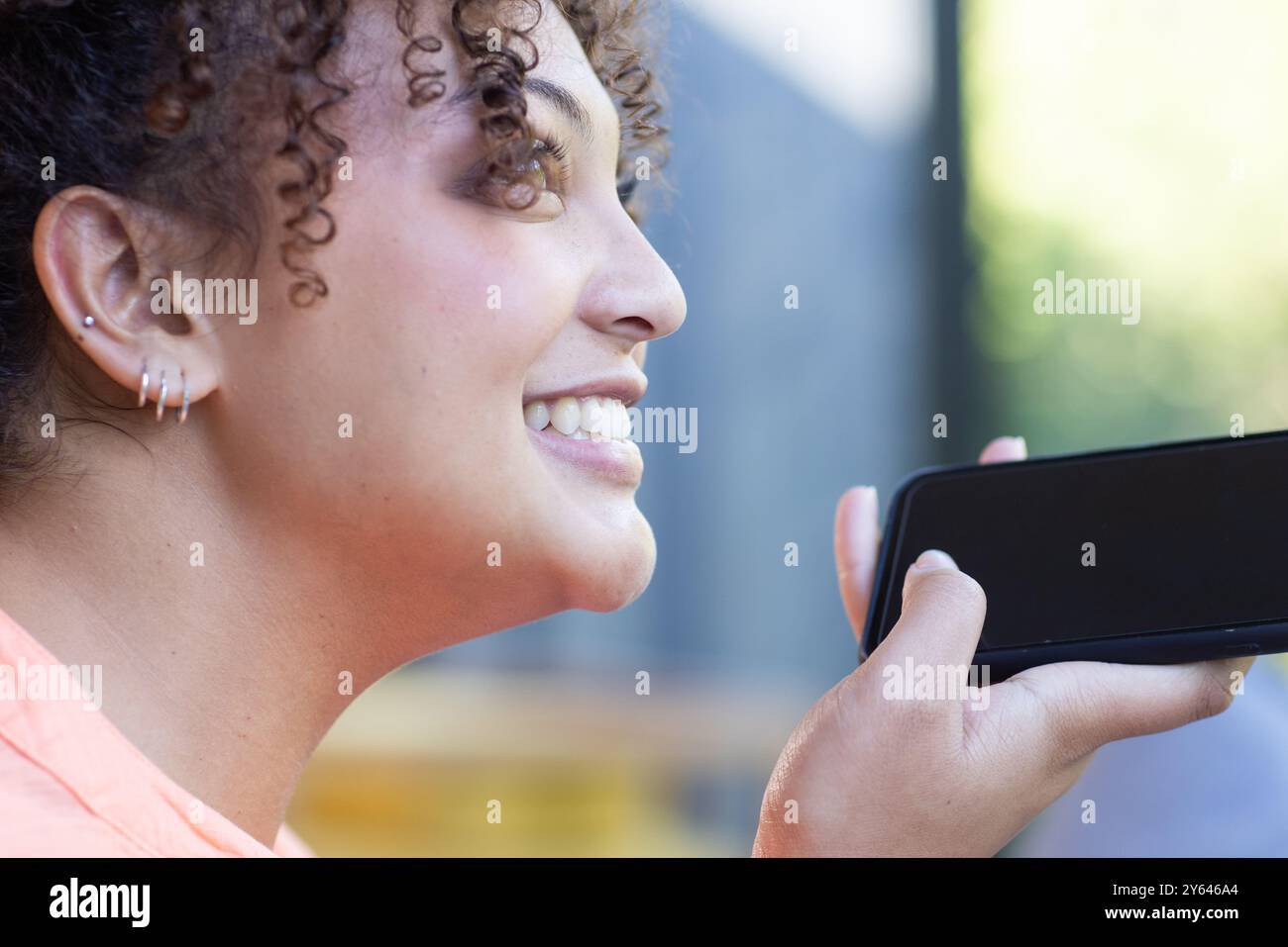 Lächelnde Frau, die ein Smartphone hält und Sprachnachrichten während Outdoor-Aktivitäten aufnimmt, zu Hause Stockfoto