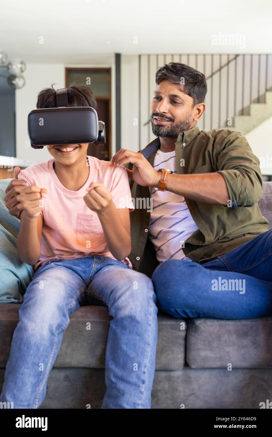 indischer Vater beobachtet den Sohn mit VR-Headset, während er zu Hause auf der Couch sitzt Stockfoto