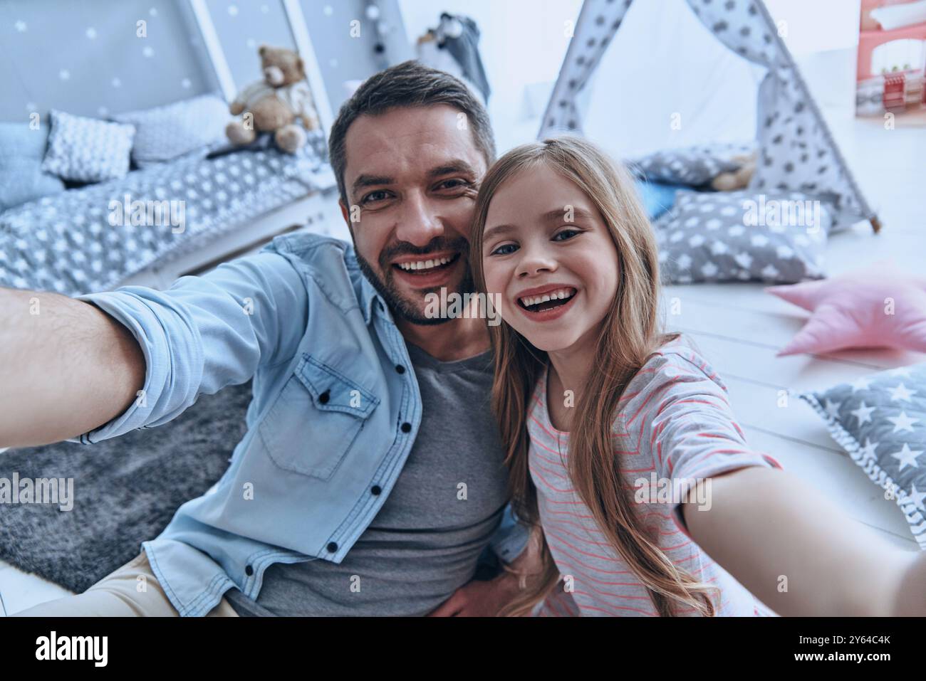 Familie ist das Wichtigste. Selbstporträt des jungen Vaters und seiner kleinen Tochter lächelnd, während sie auf dem Boden im Schlafzimmer mit dem Zelt saßen Stockfoto