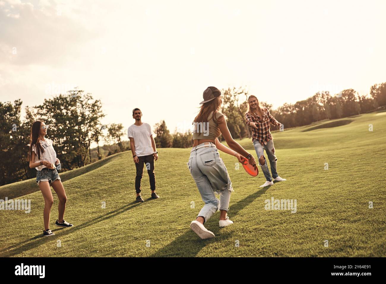 Spaß beim Spielen mit Freunden. Junge lächelnde Menschen in Freizeitkleidung spielen Frisbee, während sie unbeschwerte Zeit im Freien verbringen Stockfoto