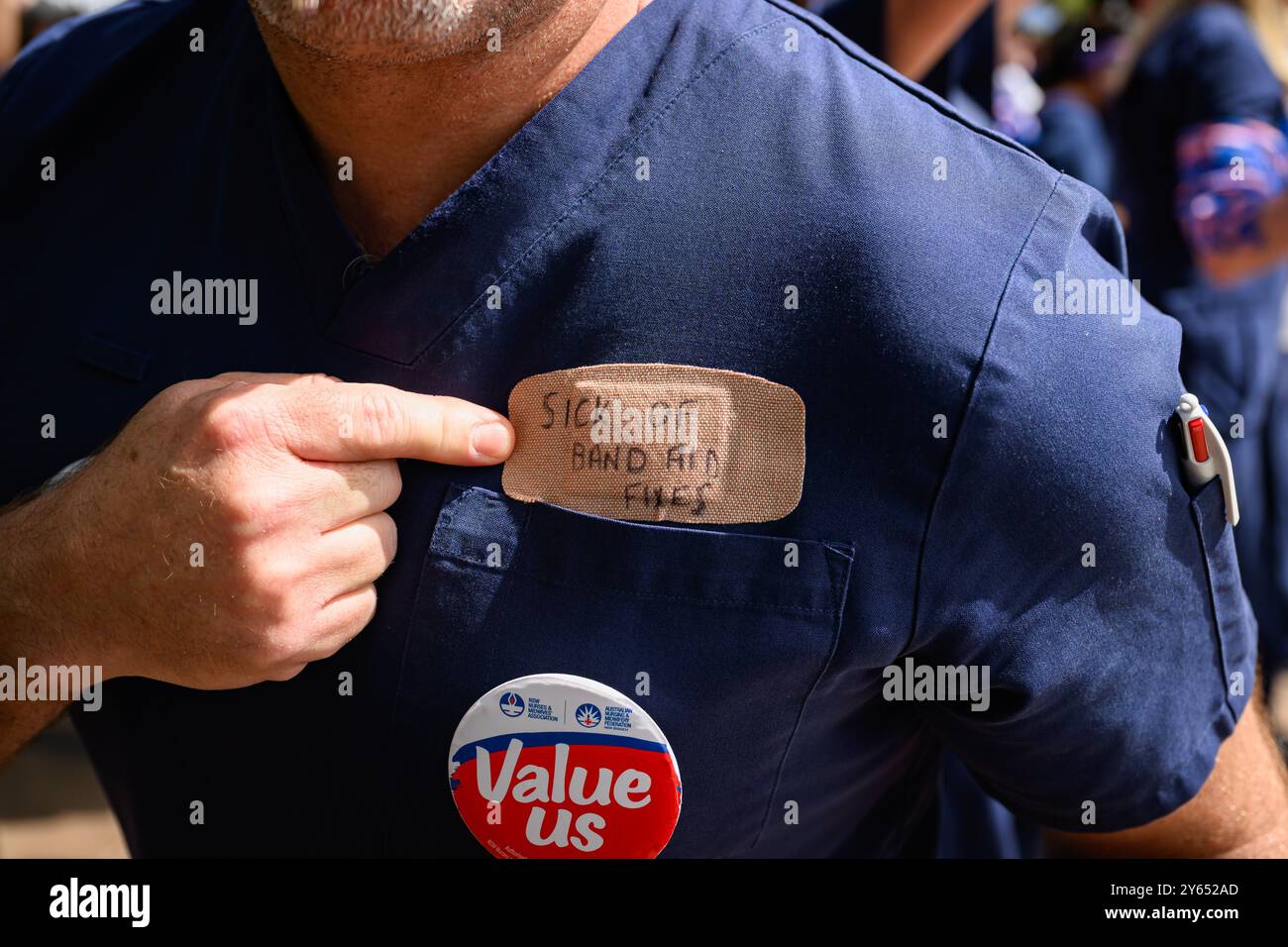 Sydney, Australien. September 2024. Ein Demonstrant sah, wie er während der Kundgebung auf das Pflaster auf seiner Brust zeigte, auf dem steht, dass es „krank von Pflasterreparaturen“ war. Krankenschwestern und Hebammen in ganz New South Wales streikten 24 Stunden und marschierten vom Hyde Park durch Sydneys Straßen zum Parlament in New South Wales und forderten eine bessere Gehaltserhöhung. Der Verband fordert eine Lohnerhöhung von 15 %, während die Regierung nur 3 % angeboten hat. (Foto: George Chan/SOPA Images/SIPA USA) Credit: SIPA USA/Alamy Live News Stockfoto