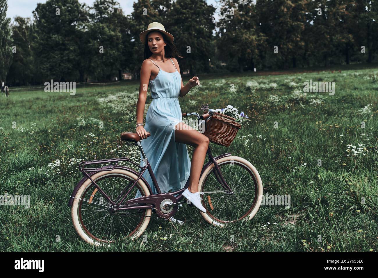 Zeit, von allem wegzukommen... Die ganze Länge einer attraktiven jungen Frau im Kleid, die wegschaut, während sie sich auf ihr altmodisches Fahrrad stützt Stockfoto