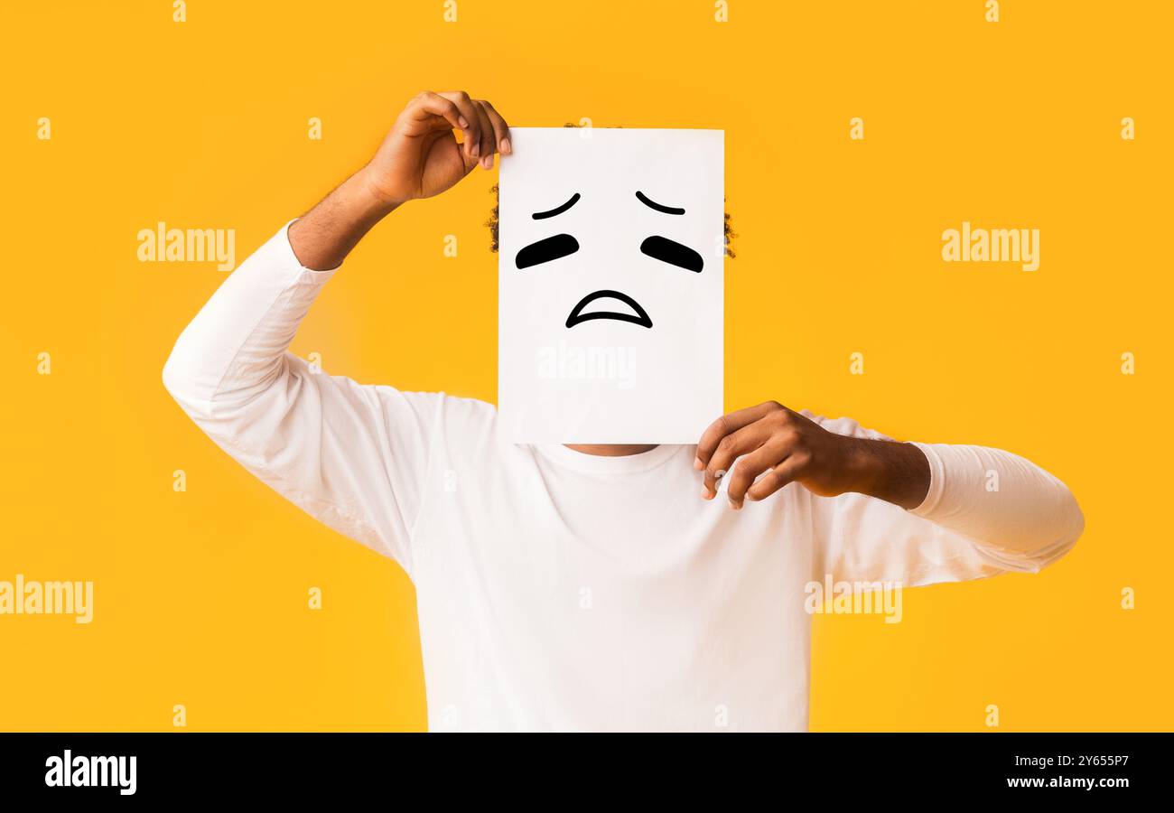 Schwarzer Mann, Papier mit traurigen Emoji über sein Gesicht Stockfoto
