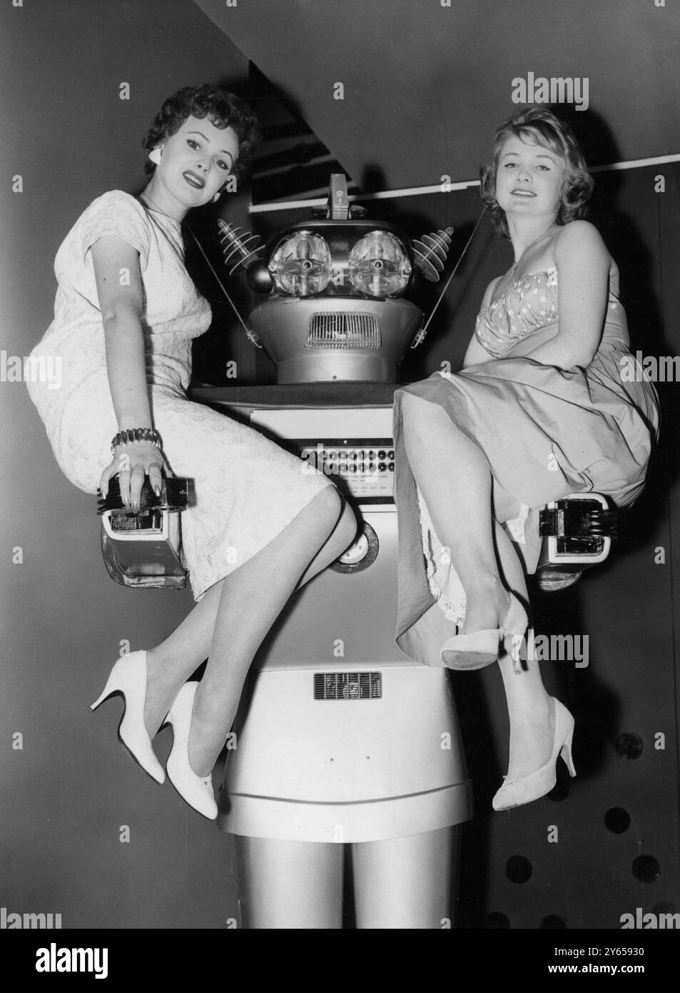 Auf den mächtigen Armen von Gygan , einem 9 ft Mechanical man , in Olympia , London , sitzen Windmill Girls Yvette Davies , 19 , von St Albans (links) und Sandra Penders , 17 , aus Blackpool . Gygan , der aus Italien kommt , ist bei Olympia , um auf der britischen Lebensmittelmesse seine elektronischen Fähigkeiten zu demonstrieren . Der von Signor P Fiorito aus Mailand erfundene Roboter wiegt 1250 Pfund . Er kann laufen, reden und praktisch jeden Auftrag ausführen . August 1958 Stockfoto
