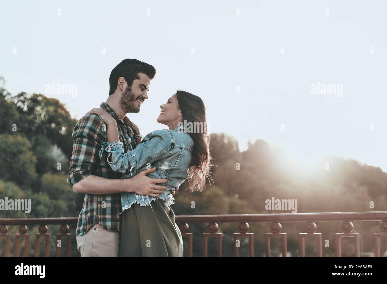 Liebe auf den ersten Blick. Wunderschönes junges Paar, das sich umschließt und ansieht, während es draußen auf der Brücke steht Stockfoto