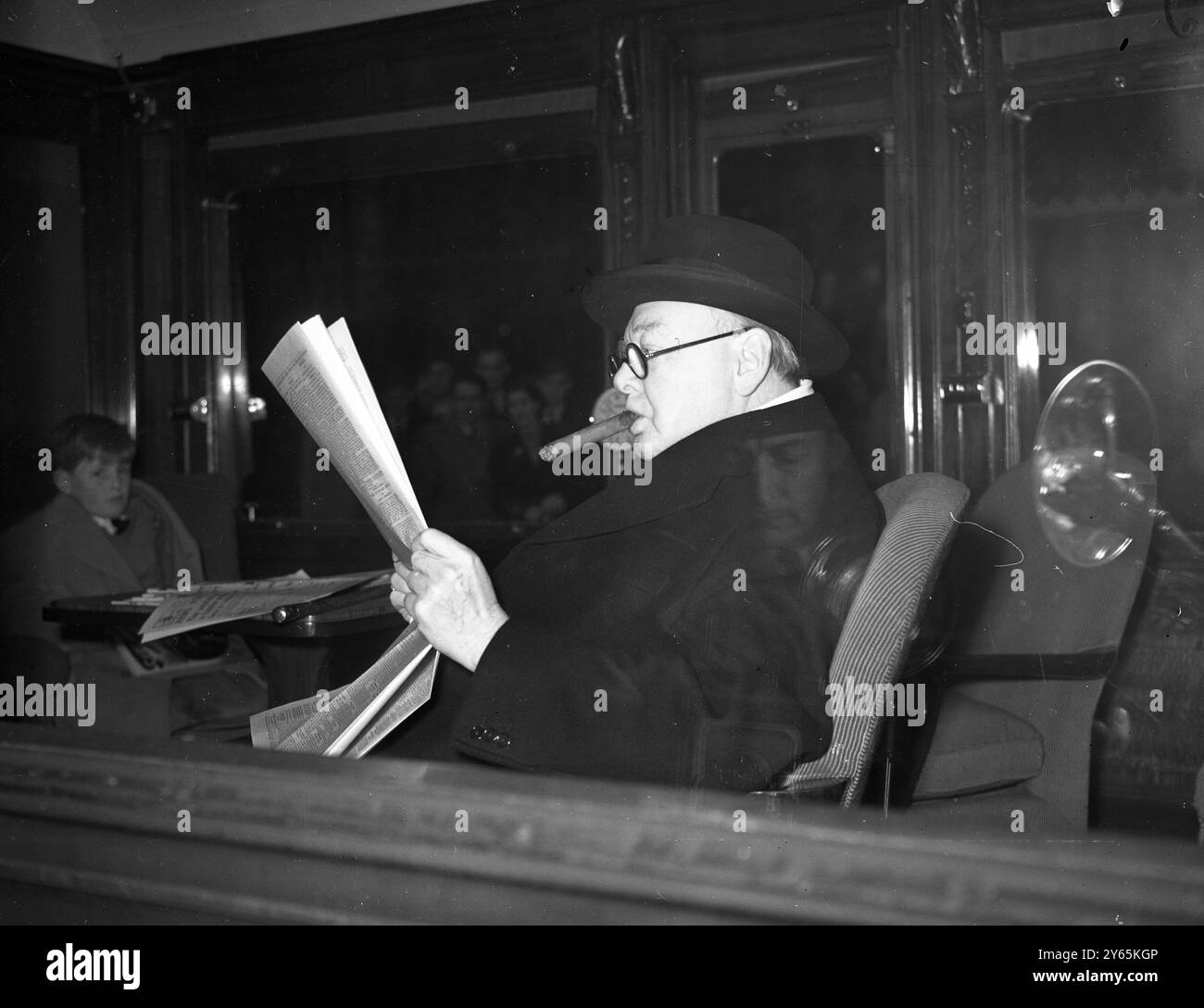 Tory Leader Geht Nach Plymouth . Der konservative Führer Winston Churchill trägt eine Brille und bläst die unvermeidliche Zigarre an , während er auf die Abfahrt seines Zuges vom Bahnhof Paddington wartet . Oktober 1951 Stockfoto