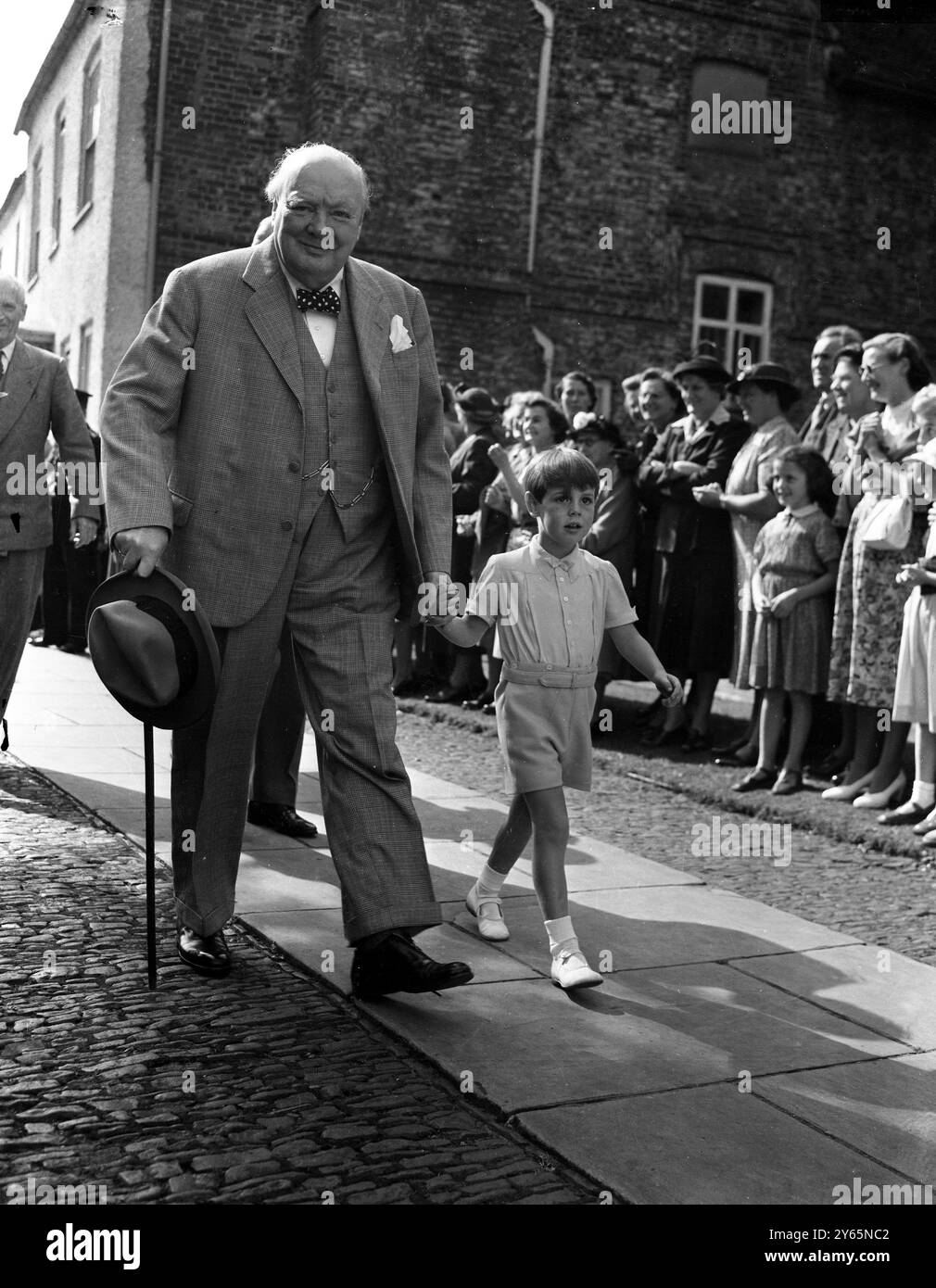 Westerham , Kent : Smiling , Herr Winston Churchill , der Premierminister , geht Hand in Hand mit seinem Enkel Nicholas Soames , während er an der Taufe von Jeremy Bernard Soames , dem zwei Monate alten achten Enkel des Premierministers , in der Westerham Parish Church teilnimmt . Das Baby ist der Sohn der Tochter des Premierministers Mary und des Hauptmanns Christopher Soames . August 1952 Stockfoto