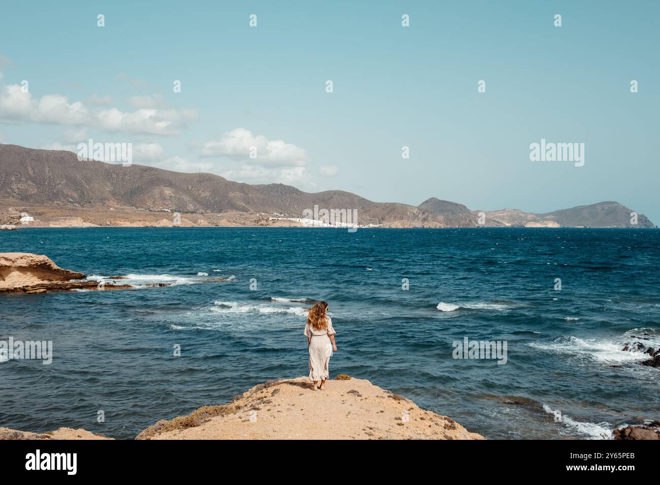 Rückansicht einer nicht erkennbaren Frau, die ein weißes Kleid trägt, mit Blick auf das Mittelmeer am Strand, Cabo de Gata, Almeria, Spanien. Stockfoto
