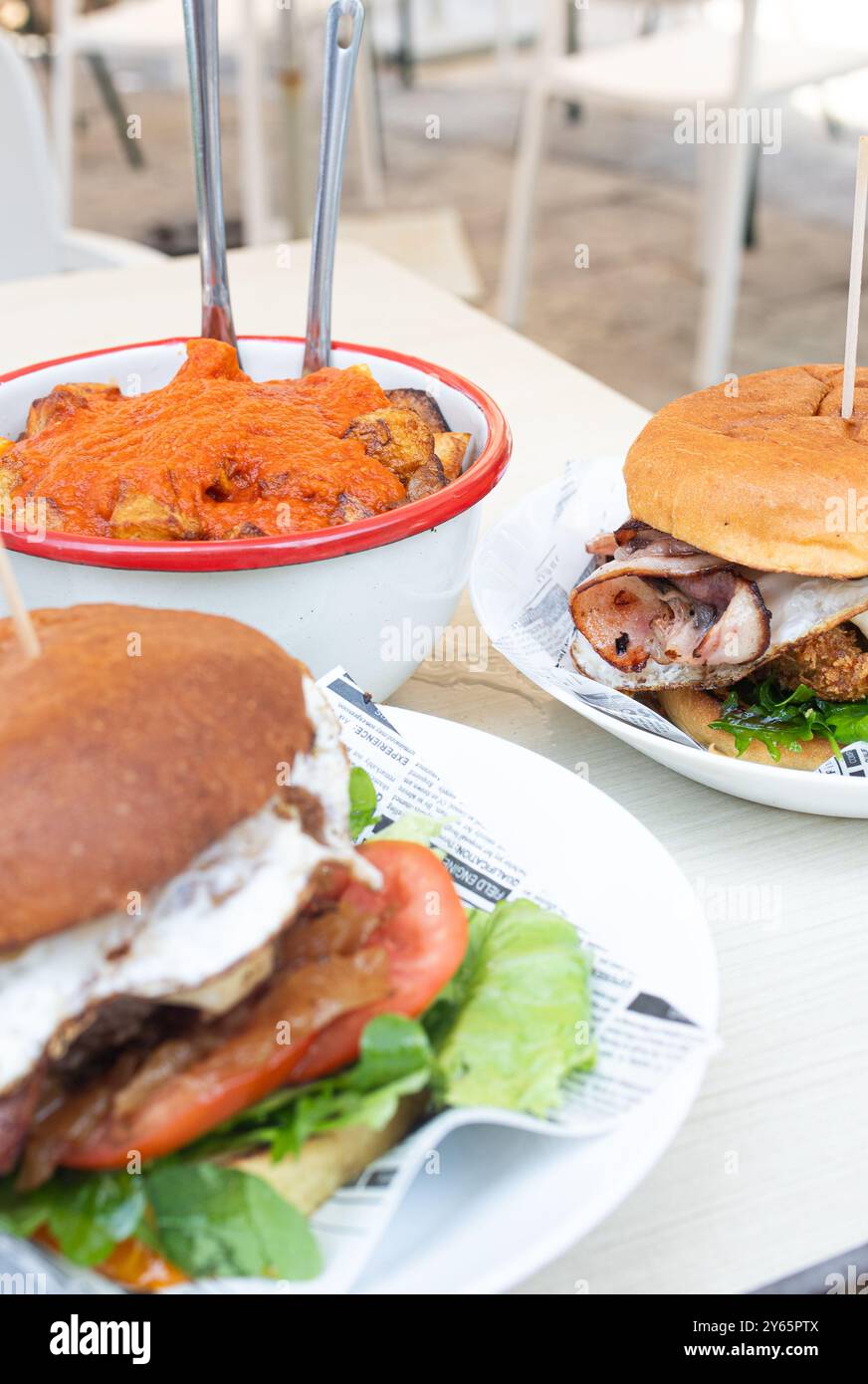 Eine köstliche Auswahl an herzhaften Burgern und einem Teller Pommes Frites mit Ketchup, die auf einem Tisch in einem zwanglosen Essbereich im Freien stehen und verschiedene fla hervorheben Stockfoto