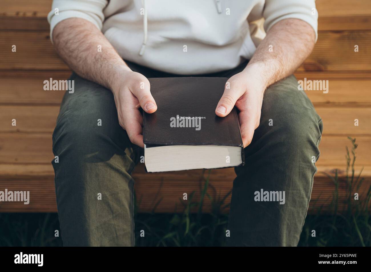 Zugeschnittene Ansicht eines nicht erkennbaren Mannes, der draußen sitzt, eine Bibel hält und liest. Stockfoto Zugeschnittene Ansicht eines nicht erkennbaren Mannes, der draußen sitzt, eine Bibel hält und liest. Stockfoto