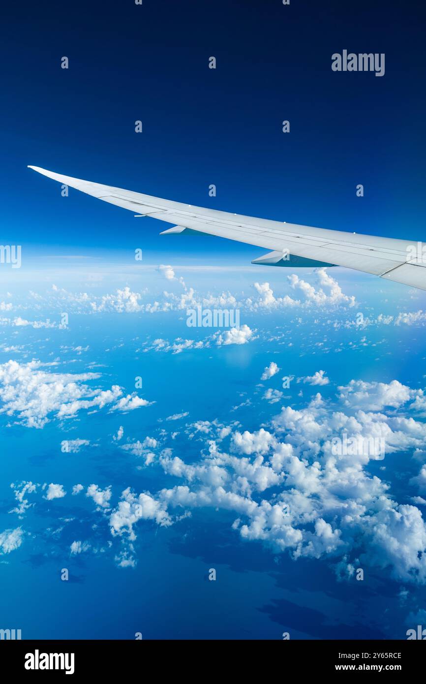 Fesselnder Blick aus der Luft auf den ruhigen blauen Himmel und die flauschigen Wolken aus der Sicht eines Flugzeugfensters, der die Flügelspitze zeigt. Stockfoto