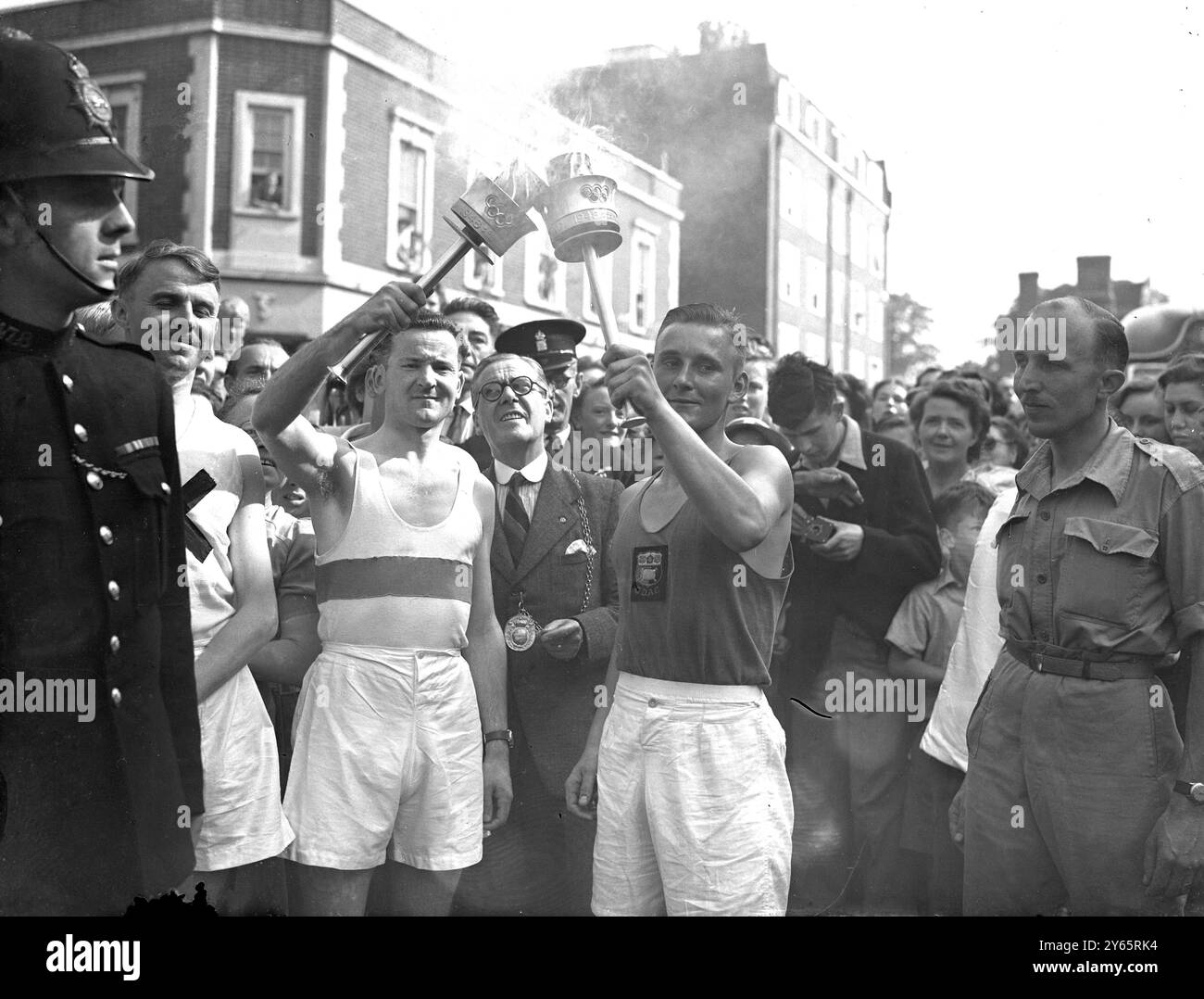 Die Straßen von Guildford säumten Menschenmassen , um zu sehen , wie die olympische Fackel von einem Staffel zum anderen übergeben wurde , um die Fackel auf ihrer Reise nach Wembley zur Eröffnung der Olympischen Spiele durch HM den König zu beschleunigen . Fotoshows: 27 Meilen bis zu gehen. Frank Ede (Dennis A.C.) (links) übernimmt die olympische Fackel von Austin Playford (Godalming A.C.), während der Bürgermeister von Guildford, Baumeister Arthur Williams, auf die Zeremonie am 29. Juli 1948 blickt Stockfoto