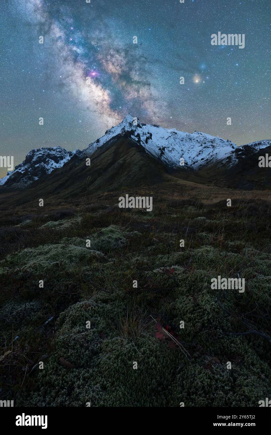 Fesselndes Bild der Milchstraße, die den Nachthimmel über einem schneebedeckten Berg in Island beleuchtet, umgeben von üppigem Moos und zerklüfteter Terra Stockfoto