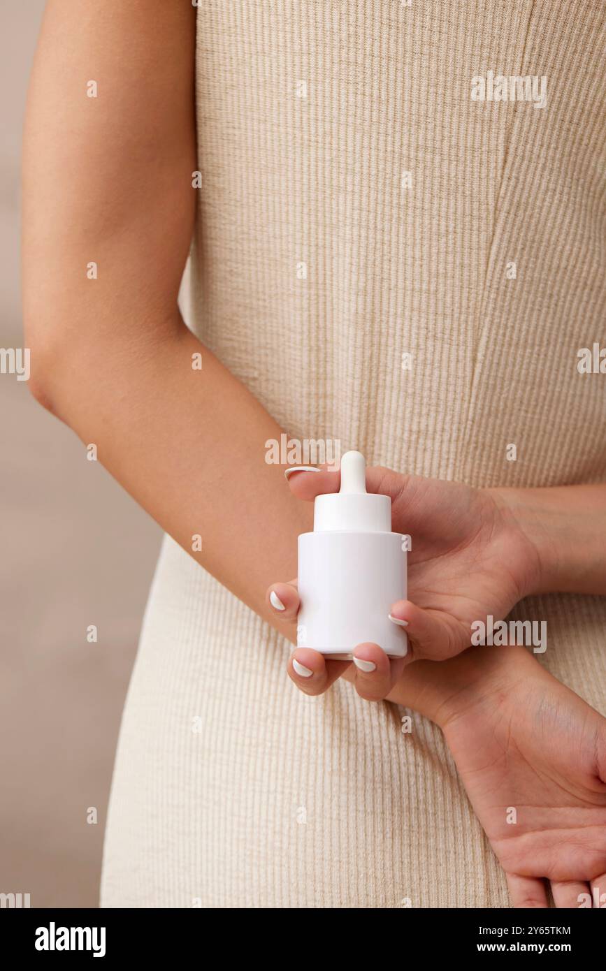 Ein Nahbild der Hände einer Frau, die eine weiße Tropfflasche Serum in der Hand hält, was die Bedeutung von Hautpflegeroutinen unterstreicht Stockfoto