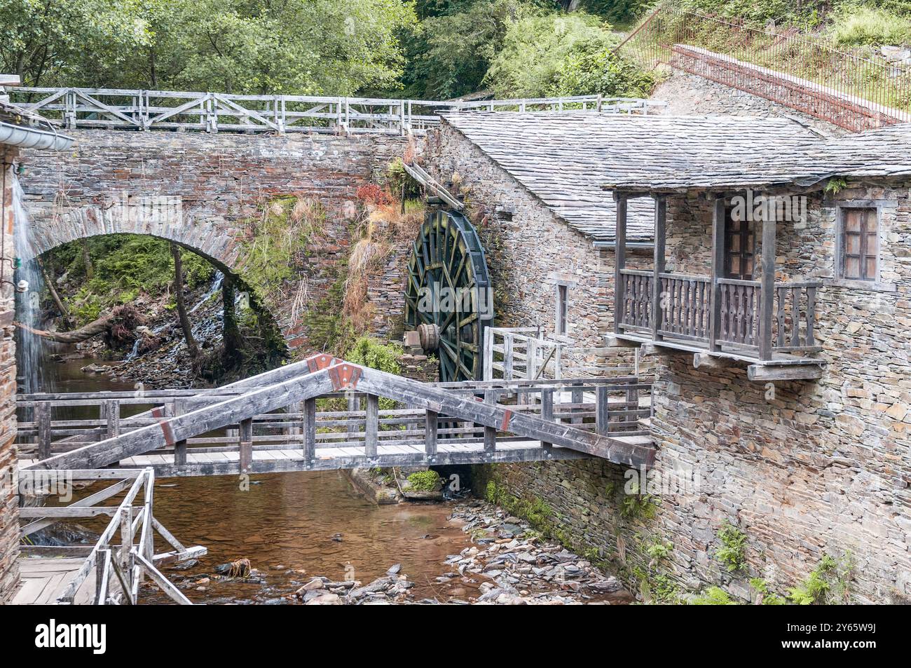 Alte Wassermühle mit einem großen Wasserrad, moosigen Steinmauern und einer bewaldeten Umgebung zeigt das Bild die komplizierte Architektur der Mühle und Stockfoto