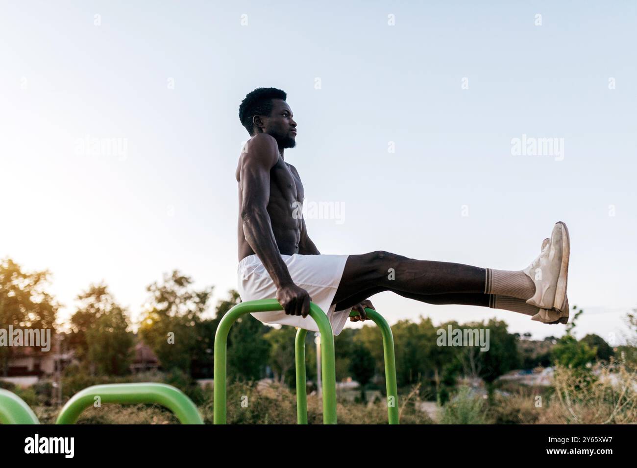 Ein fitter Mann, der seinen Körper zeigt, trainiert Calisthenics mit parallelen Bars in einem ruhigen Park während des Sonnenuntergangs und spiegelt ein ruhiges und doch kraftvolles Workout wider Stockfoto