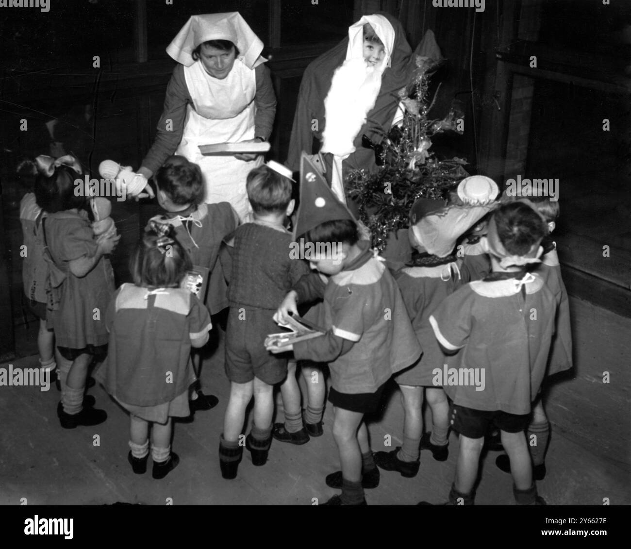Kinder in einem Kindergarten für Kinder unter fünf Jahren, deren Väter hauptsächlich in der Armee sind und ihre Mütter arbeiten. Eine Krankenschwester überreicht Weihnachtsgeschenke an eifrige Kinder. Dezember 1940 Stockfoto
