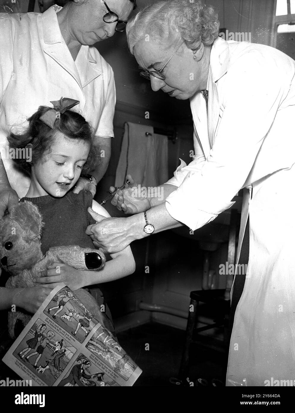 Hendon Middlesex : der sechsjährige Marian Fisher, der einen Teddybären und einen Comic umklammert, sieht sich einer Polio-Impfung gegenüber, die von Dr. K M Bodkin, dem Area Medical Officer des Middlesex County Council, in der Central Clinic, Hendon, verabreicht wurde. Die ersten Injektionen des Polio-Impfstoffes werden Kindern in der Grafschaft Middlesex in verschiedenen Kliniken verabreicht. Von der geschätzten Zahl von 247.000 Kindern, die in Middlesex in Frage kommen, wurden etwa 32 % für eine Injektion registriert.8. Mai 1956 Stockfoto