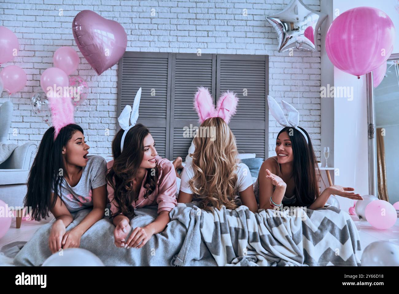 Süßer als jeder Hase. Vier schöne junge Frauen in Hasenohren, die eine tolle Zeit haben, während sie auf dem Bett liegen Stockfoto
