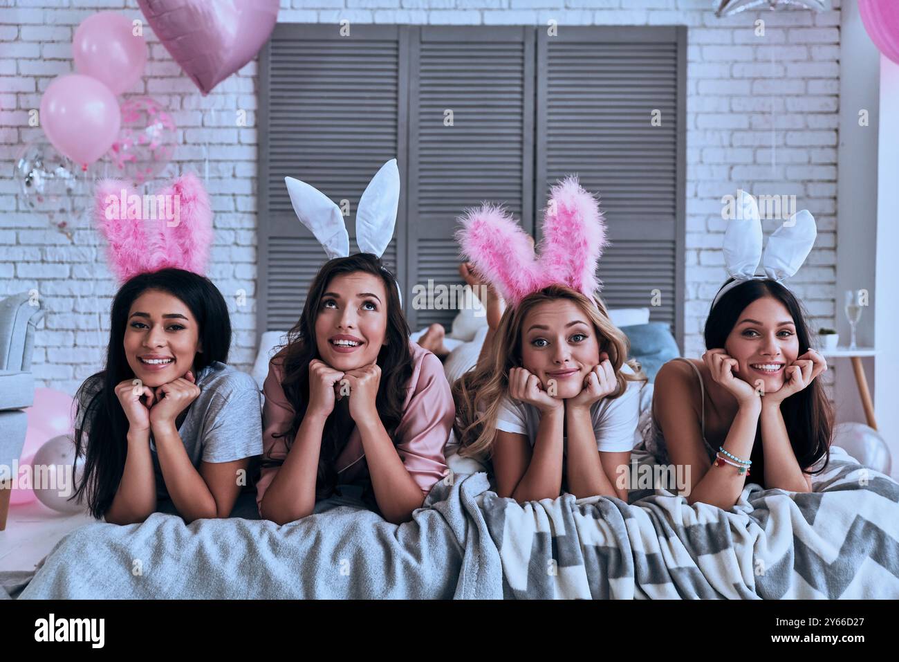 Schönheiten pur. Vier attraktive junge Frauen in Hasenohren lächeln, während sie auf dem Bett liegen Stockfoto