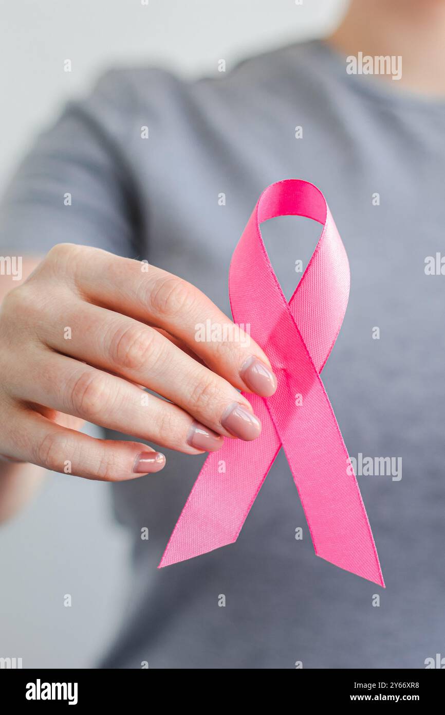 Frau in grauem T-Shirt hält rosa Schleife in den Händen. Mamma Cancer Awareness Month. Unterstützung und Förderung von Kampagnen gegen Krebs. Gesundheitskonsum Stockfoto
