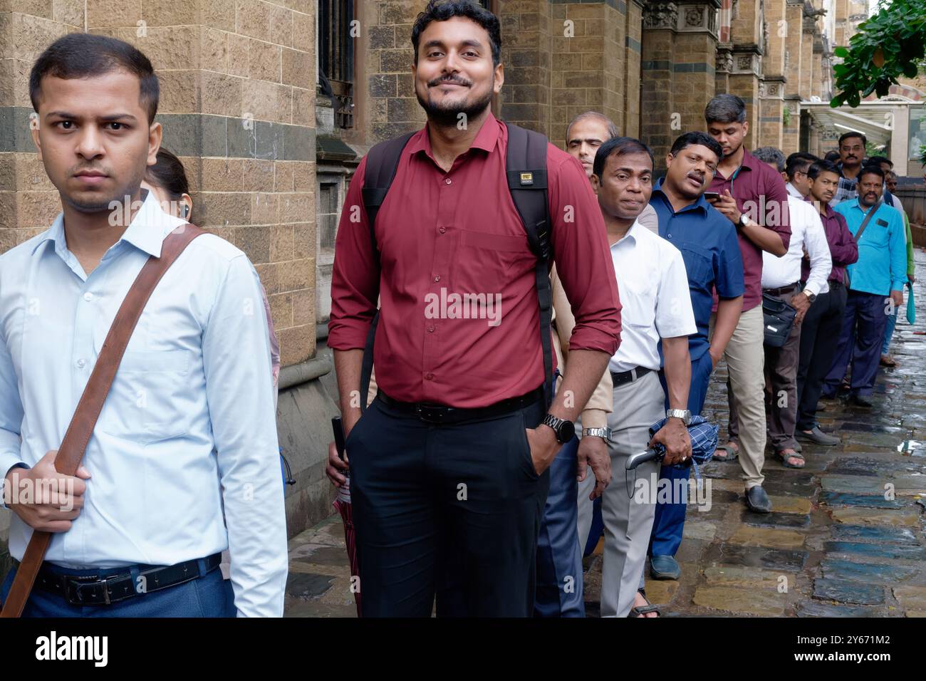 Männliche Pendler stehen in einer geordneten Buswarteschlange vor dem Chhatrapati Shivaji Maharaj Terminus in Mumbai, Maharashtra, Indien Stockfoto
