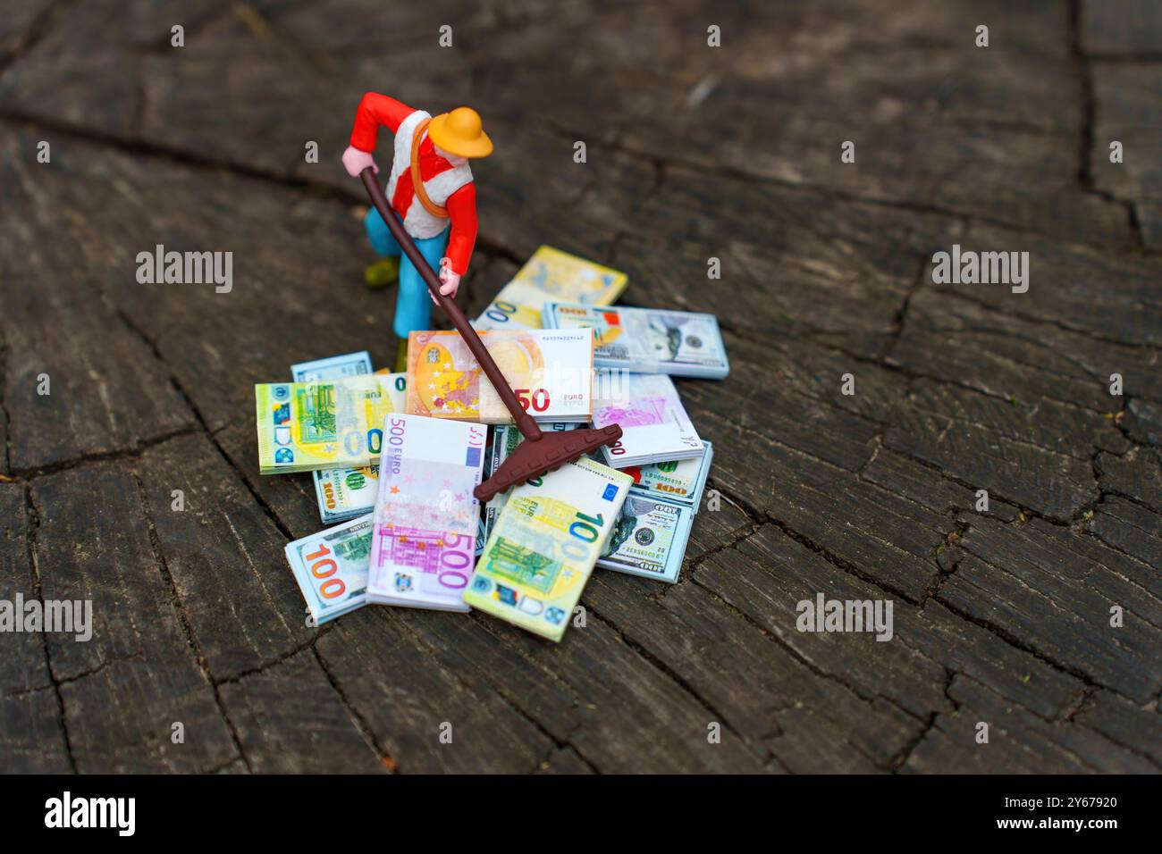 Miniaturgärtner, der mit einem Rechen Geld sammelt, repräsentiert finanzielle Betreuung und Wachstumsorientierung. Stockfoto