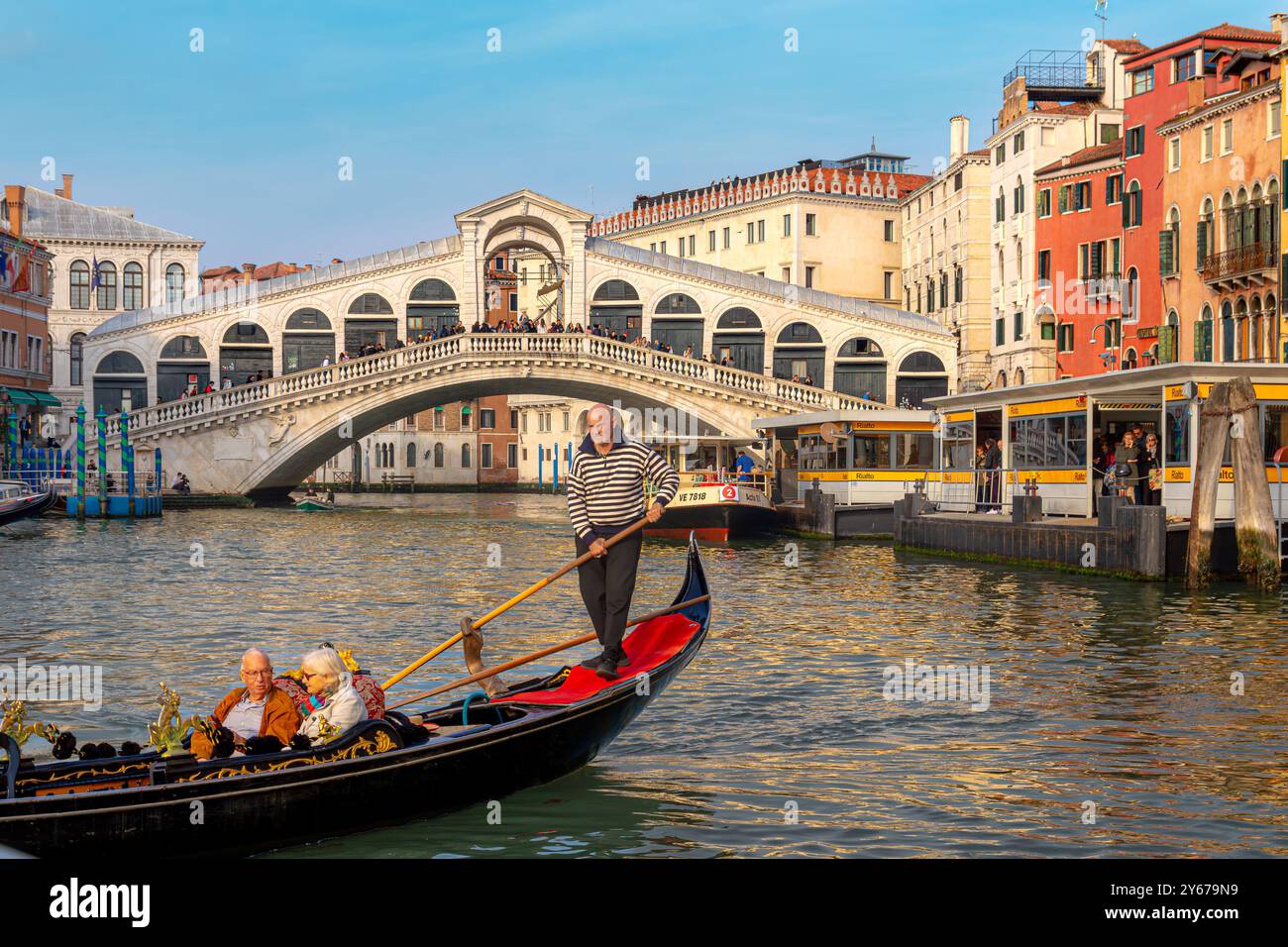 Ein Coupé, das eine Gondelfahrt macht, während ein Gondolierer seine Gondelfahrt entlang des Canal Grande in der Nähe der Rialtobrücke in Venedig, Italien, führt Stockfoto