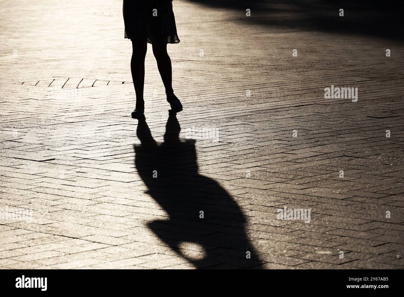 Schwarze Silhouette und Schatten einer einsamen, schlanken Frau, die auf einer Straße läuft. Weibliche Beine im Herbst auf dem Bürgersteig Stockfoto