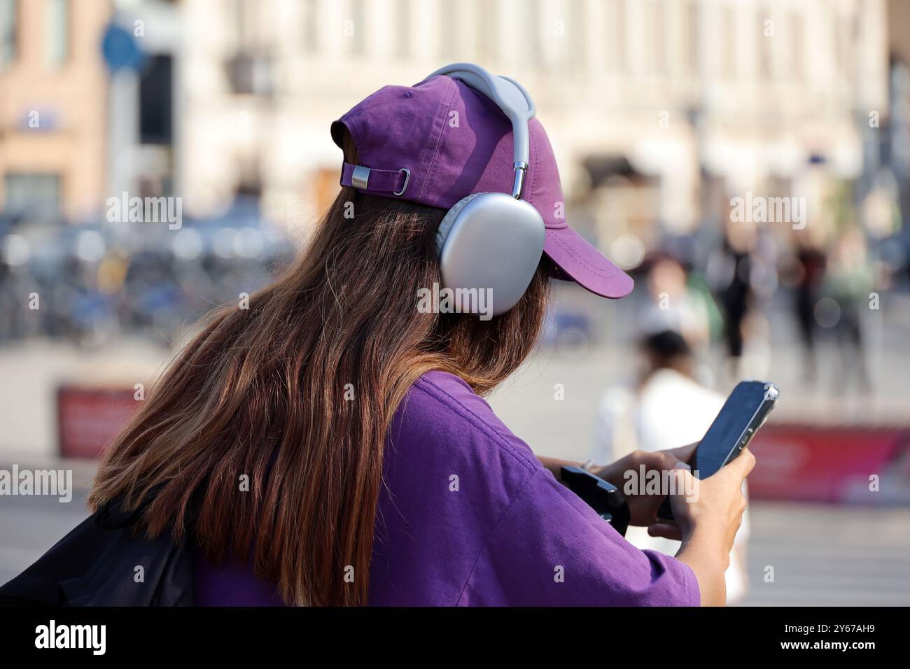 Mädchen in Kopfhörern mit Smartphone auf einer Straße in der Stadt vor dem Hintergrund von Menschen Stockfoto