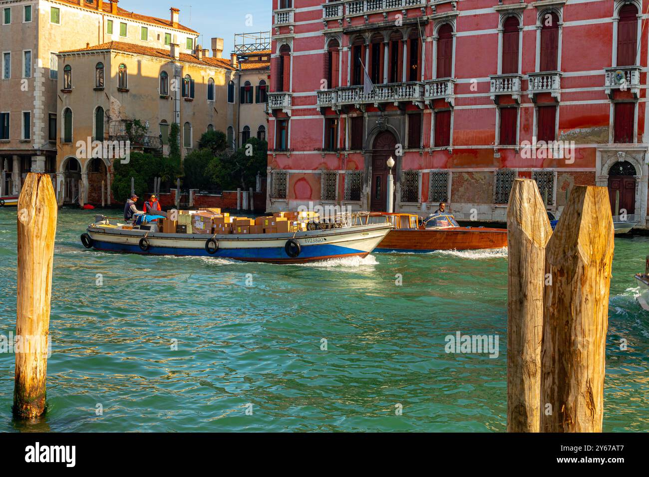 Ein motorisiertes Handelsboot mit Waren und einem Wassertaxi auf dem Canal Grande in Venedig, Italien Stockfoto