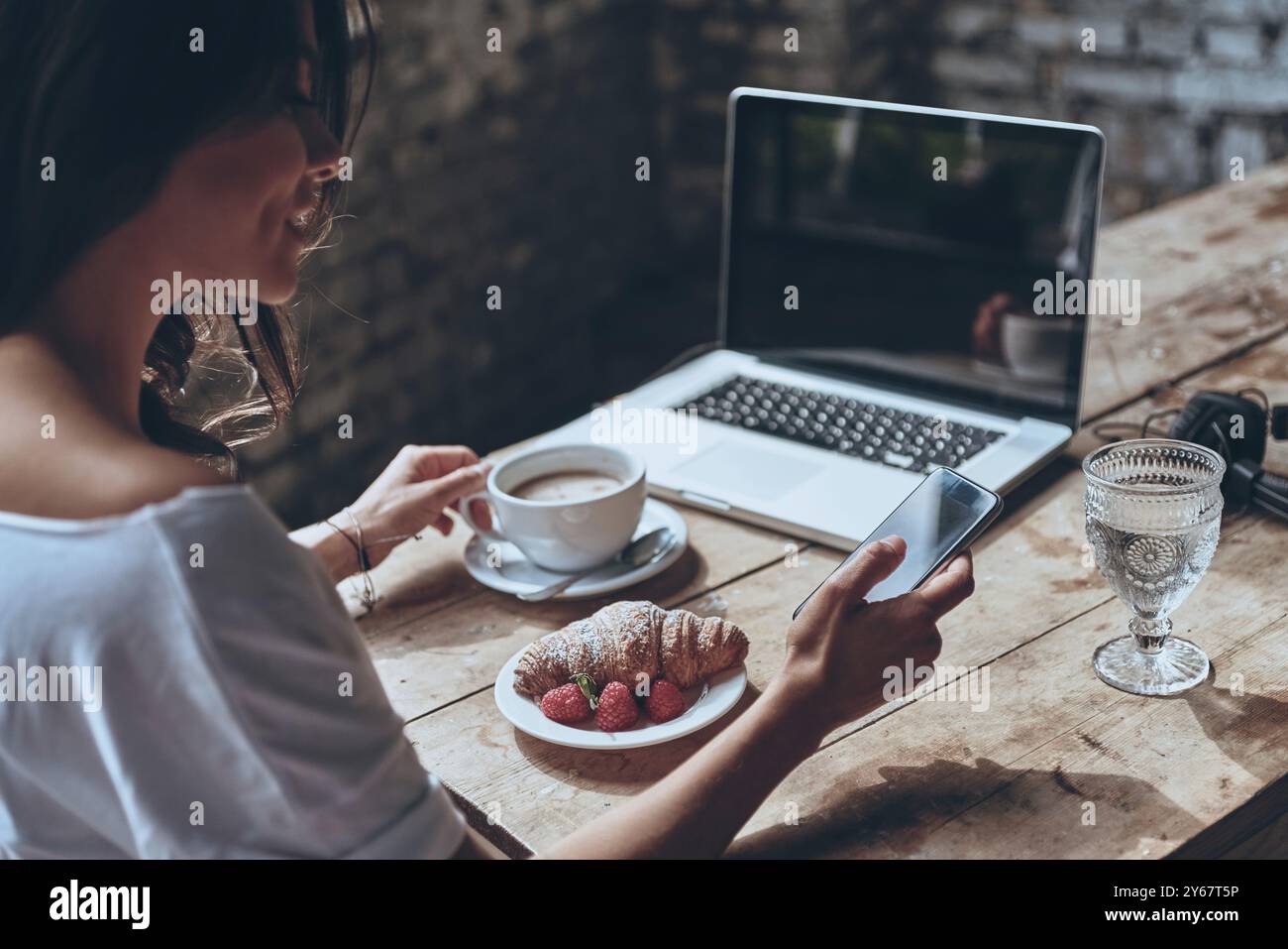 Kurzer Chat am Morgen. Rückansicht einer Frau, die ihr Smartphone benutzt, während sie zu Hause frühstückt Stockfoto