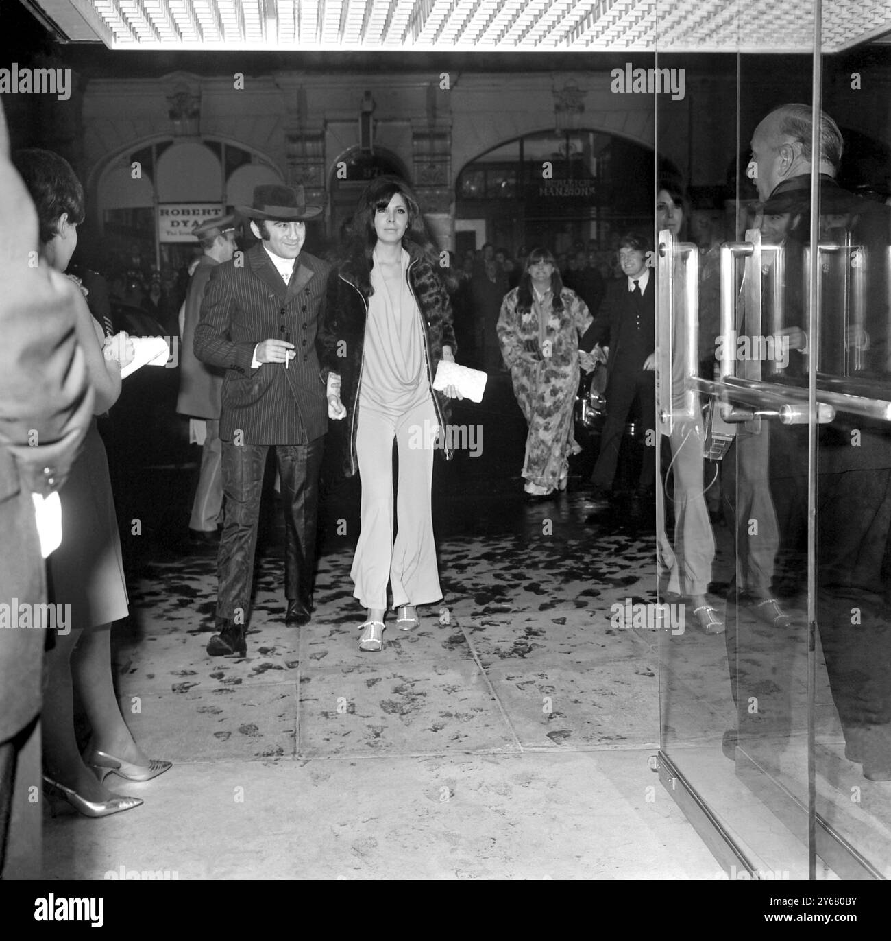 Lionel Bart und sein Gefährte Sharon Sheeley kommen zur Premiere von "Durchschnittlich modern Millie". Lionel trug einen gestreiften, hoch geknöpften zweireihigen Mantel mit Revers und Taschenklappen, die zu seiner Hose passen. Sharon trägt am 13. Oktober 1967 einen weißen Pyjama-Hosenanzug mit tiefem Ausschnitt Stockfoto