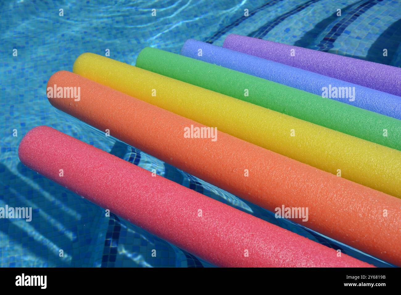 Regenbogenfarbene Poolnudeln, die in einem Swimmingpool schwimmen, Sommerspaß-Konzept Stockfoto