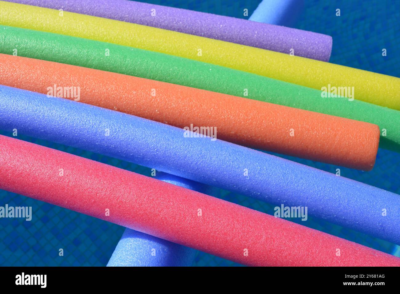 Regenbogenfarbene Poolnudeln, die in einem Swimmingpool schwimmen, Sommerspaß-Konzept Stockfoto