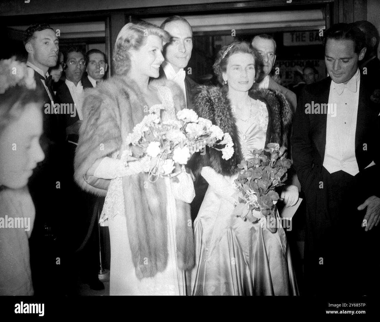 Rita Hayworth, die Filmschauspielerin, besuchte die Uraufführung ihres Films Down To Earth im Gaumont Theatre in Haymarket, London, dessen Erlöse für die Unterstützung der britischen limbless Ex-Servicemens' Association bestimmt waren. Rita trat durch den Hintereingang des Theaters ein, um der großen Menge von Filmfans zu entgehen, die darauf warteten, sie zu sehen, und machte sich dann auf den Weg zum Foyer, wo sie der Herzogin von Gloucester vorgestellt wurde. Das Foto zeigt Rita Hayworth (links) mit der Herzogin von Gloucester (rechts) und Lord Willoughby (Mitte) im Gaumont zur Premiere. Juli 1947 Stockfoto