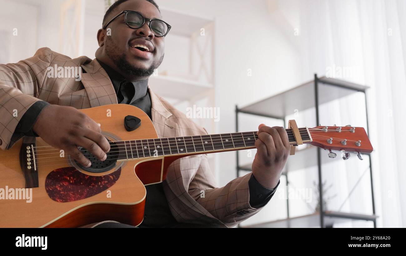 Musik-Inspiration. Gitarrist Freizeit. Liedaufführung. Talentierter emotional singender Mann, der Melodie auf akustischen Instrumenten zu Hause im Wohnzimmer spielt. Stockfoto