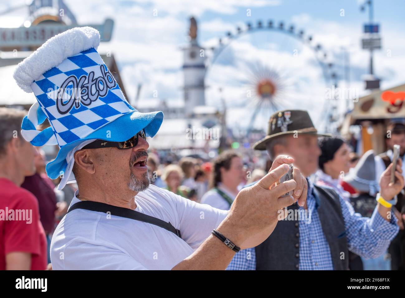 Wiesnbesucher aus Texas auf dem Oktoberfest, München, September 2024 Deutschland, München, September 2024, Tourist aus Texas mit Wiesnhut auf dem Oktoberfest, macht Erinnerungsfotos mit seinem Smartphone, blau-weißer Maßkrug Hut, US Touristen, Tourismus, Hut, typisch bayerisch, Volksfest, Bayern, *** Oktoberfest Besucher aus Texas beim Oktoberfest, München, September 2024 Deutschland, München, September 2024, Tourist aus Texas mit Oktoberfest Hut auf dem Oktoberfest, macht Souvenirfotos mit seinem Smartphone, blau-weiß Bierbecher Hut, US-Touristen, Tourismus, Hut, typisch bayerisch, Volksfest, Stockfoto