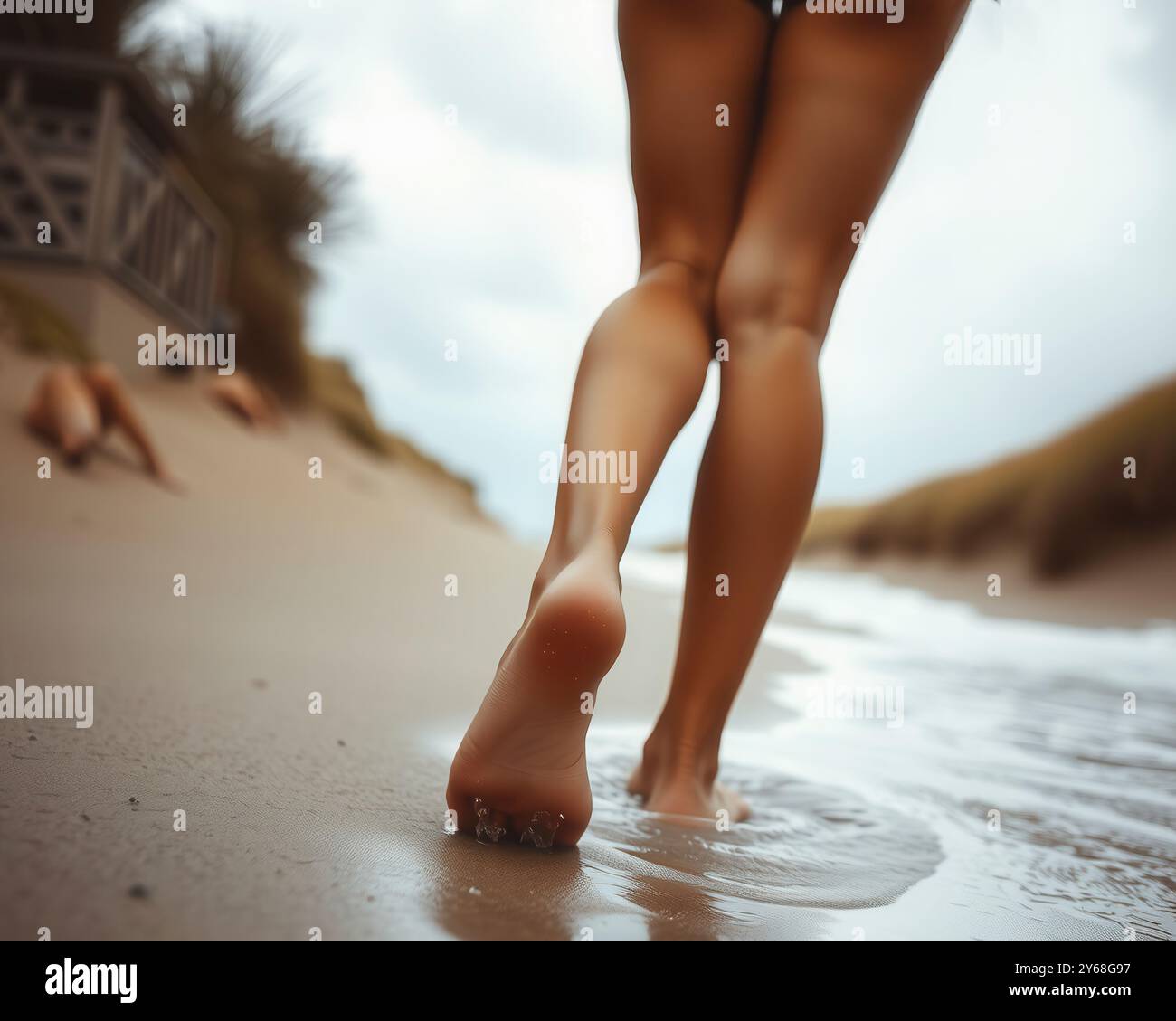 Blick auf die junge Frau, die im Bikini entlang des Strandes durch das Wasser geht – konzentrieren Sie sich auf Füße und Beine Stockfoto