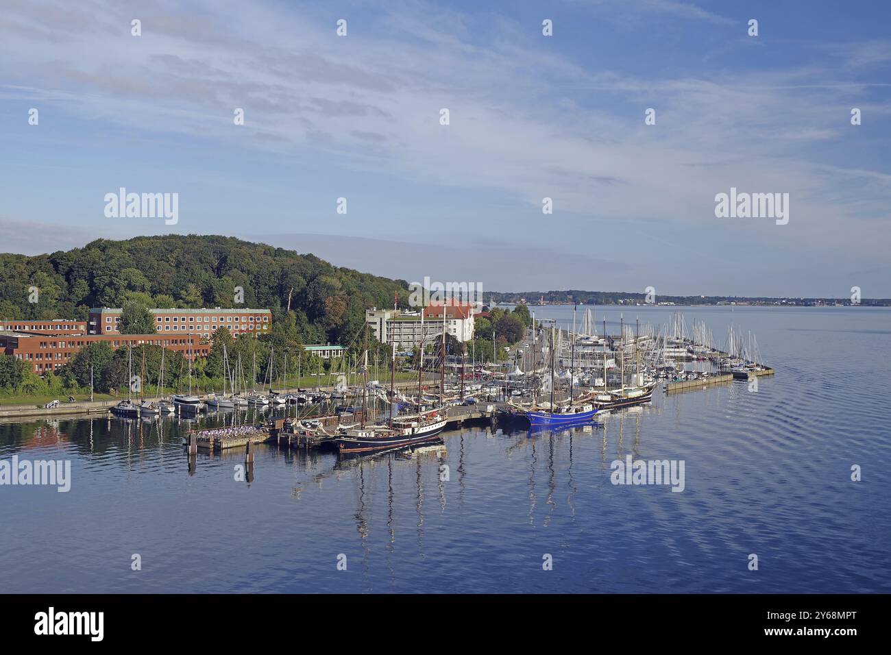 Ein Hafen voller Segelschiffe, umgeben von Gebäuden und grünen Hügeln unter blauem Himmel, Kiel-Holtenau, Kieler Fjord, Kiel, Schleswig-Holstein, Deutsch Stockfoto
