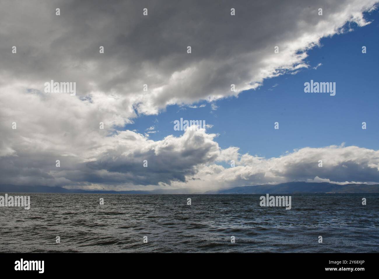 Ein Himmel voller schöner Wolken, beleuchtet von der Sonne. Davor hat es geregnet. Das plätschernde Wasser des Sees überfließt im Licht. Stockfoto