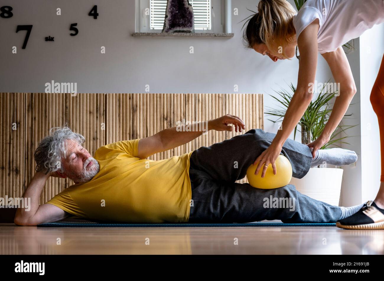 Weibliche Physiotherapeutin unterrichtet Pilates Kraftübungen mit einem Ball zu einem älteren Mann, um ihm in seiner Genesung und gesundes Altern zu helfen. Stockfoto