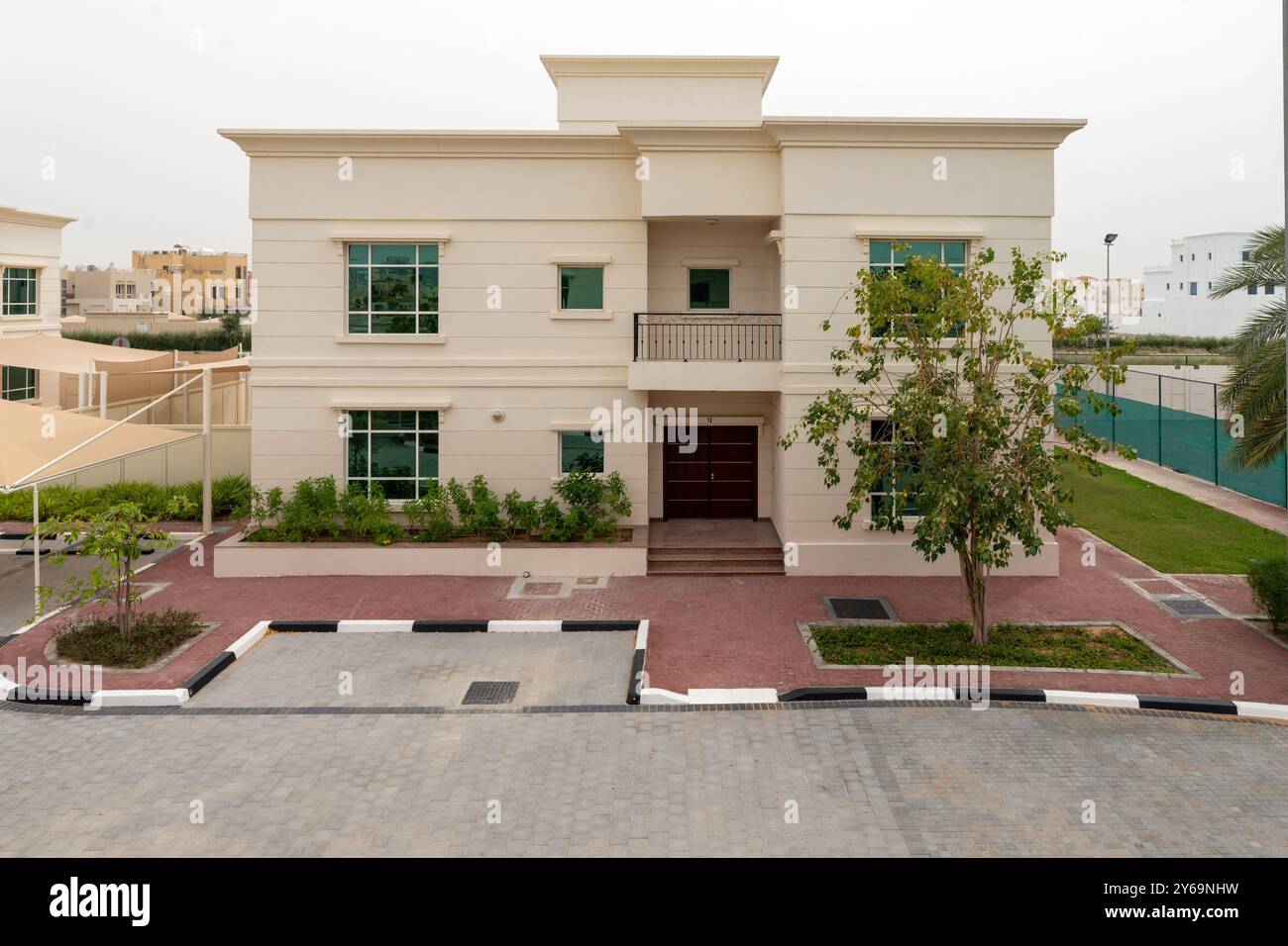 Ein modernes Gebäude in Khalifa A, Abu Dhabi. Helle Fassade, große Fenster, zentraler Eingang mit Balkon, Gartenanlage Stockfoto