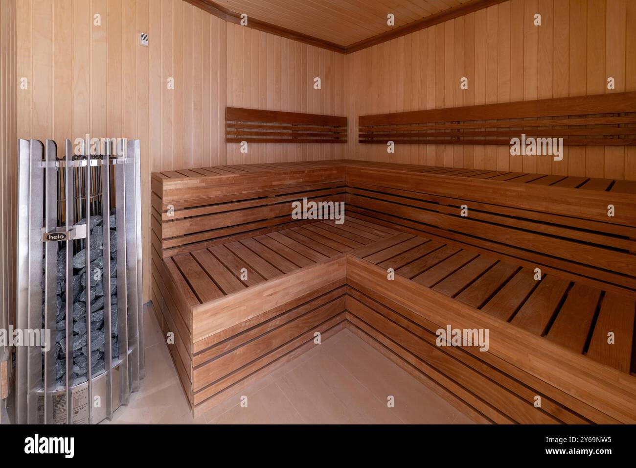 Eine hölzerne Sauna mit L-förmigen Bänken, ein Eckofen mit beheizten Steinen und ein gemütliches, entspannendes Ambiente Stockfoto