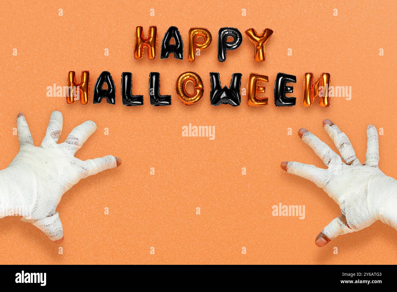 Mami Hand mit Bandagen darauf, die schwarze und orangene Ballonbuchstaben mit der Aufschrift Happy Halloween auf farbigem Hintergrund zeigen. Happy Halloween Konzept Stockfoto