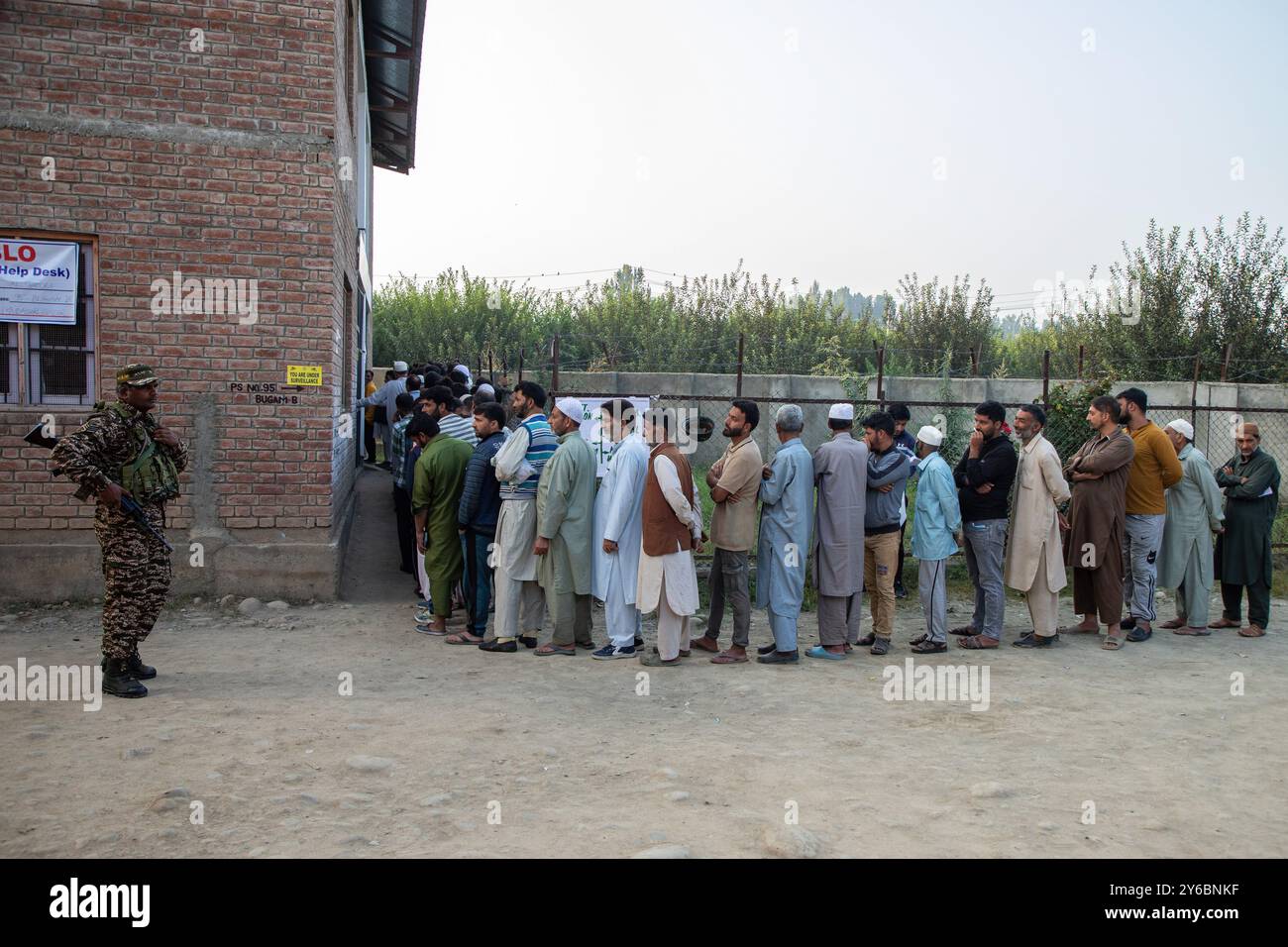 Indischer paramilitärischer Soldat steht auf der Wache, während die kaschmirischen Wähler in der zweiten Phase der Parlamentswahlen in Jammu und Kaschmir am Stadtrand von Srinagar in einer Warteschlange warten, um ihre Stimmzettel vor dem Wahlhaus abzugeben. Dies sind die ersten Kommunalwahlen seit einem Jahrzehnt und die ersten, seit Neu-Delhi 2019 den halbautonomen Status der Region widerrief und sie unter direkte Herrschaft stellte. Fast neun Millionen Menschen sind registriert, um in der umstrittenen Region zu wählen, die traditionell für Boykotte aus Protest gegen die indische Herrschaft bekannt ist. Stockfoto