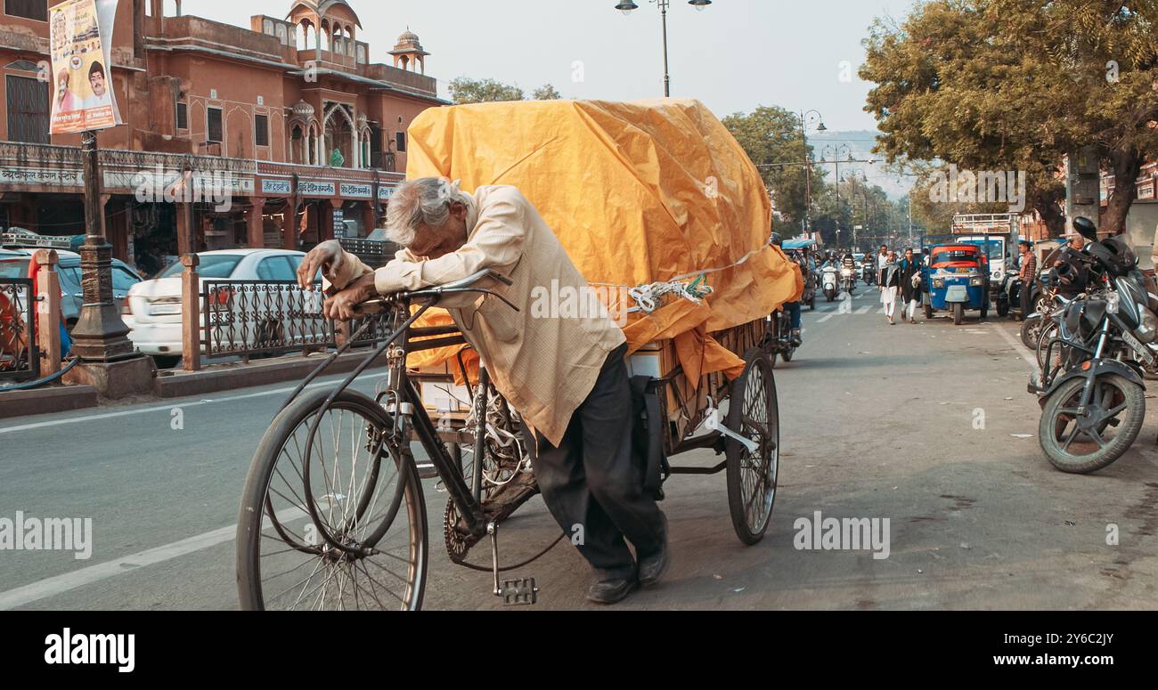 Jaipur, Rajasthan, Indien. Der alte indische Mann trägt den Wagen mit schwerem LKW. Verkehr auf der Chhoti Chopad Straße. Autos fahren abends auf der Straße. Stockfoto