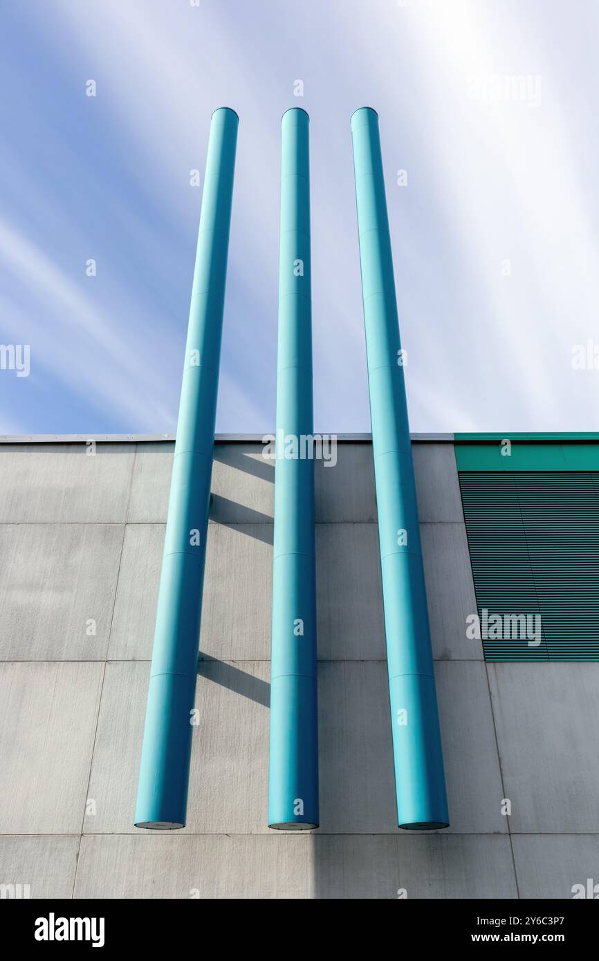 Gebäudewand mit drei türkisfarbenen vertikalen Rohren im Freien Stockfoto