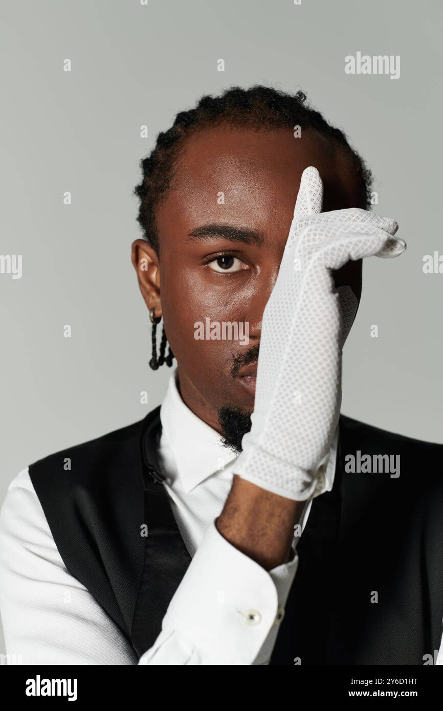 Ein junger Afroamerikaner zeigt seinen Sinn für Mode in einem eleganten Anzug und weißen Accessoires gegen Grau. Stockfoto