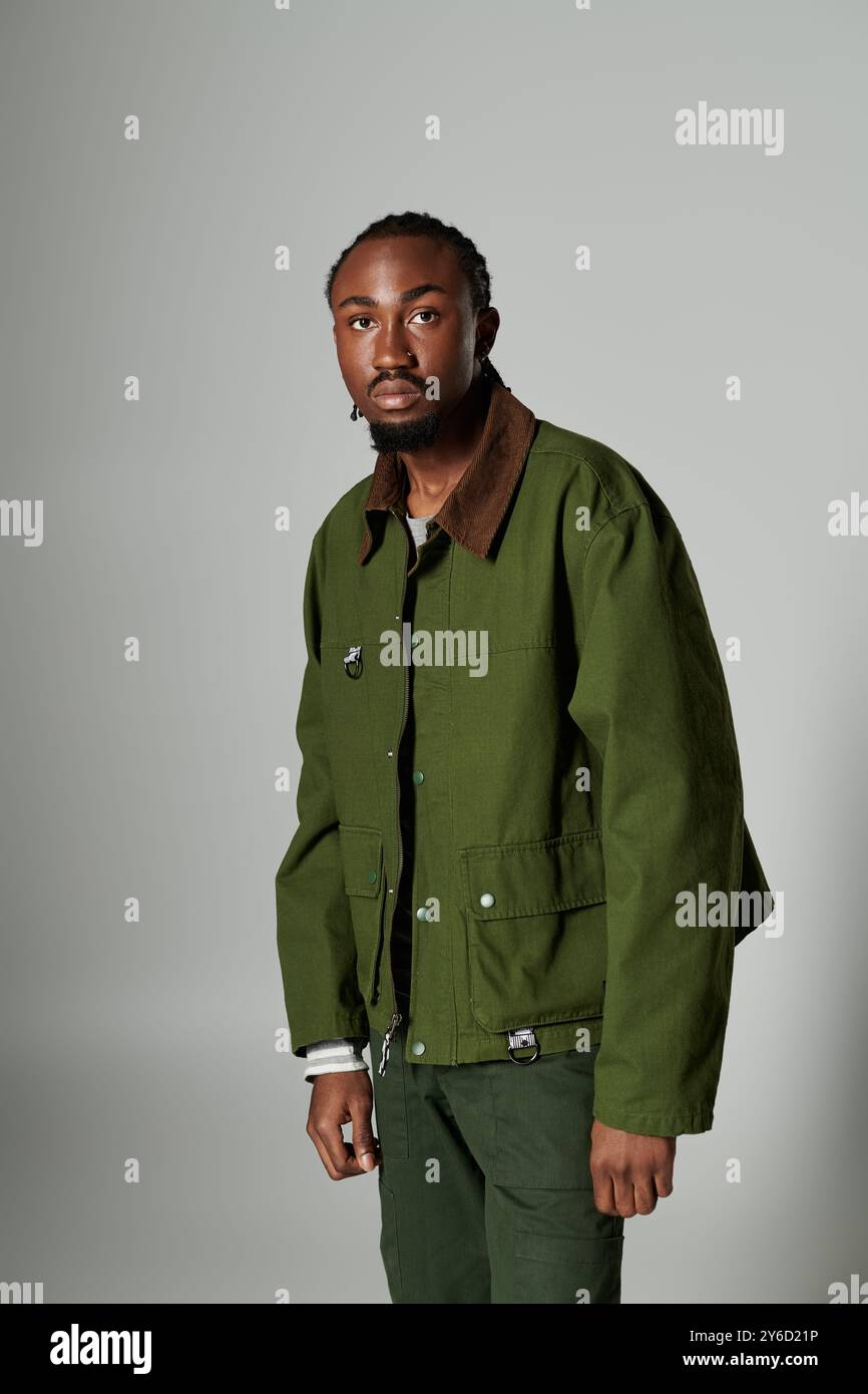 Ein junger Mann mit ausgeprägtem Modestil zeigt sein grünes Outfit und seine auffällige Präsenz an einer grauen Wand. Stockfoto